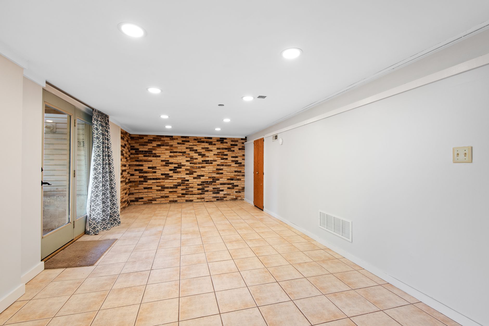 Finished basement room with a brick accent wall and a walkout door