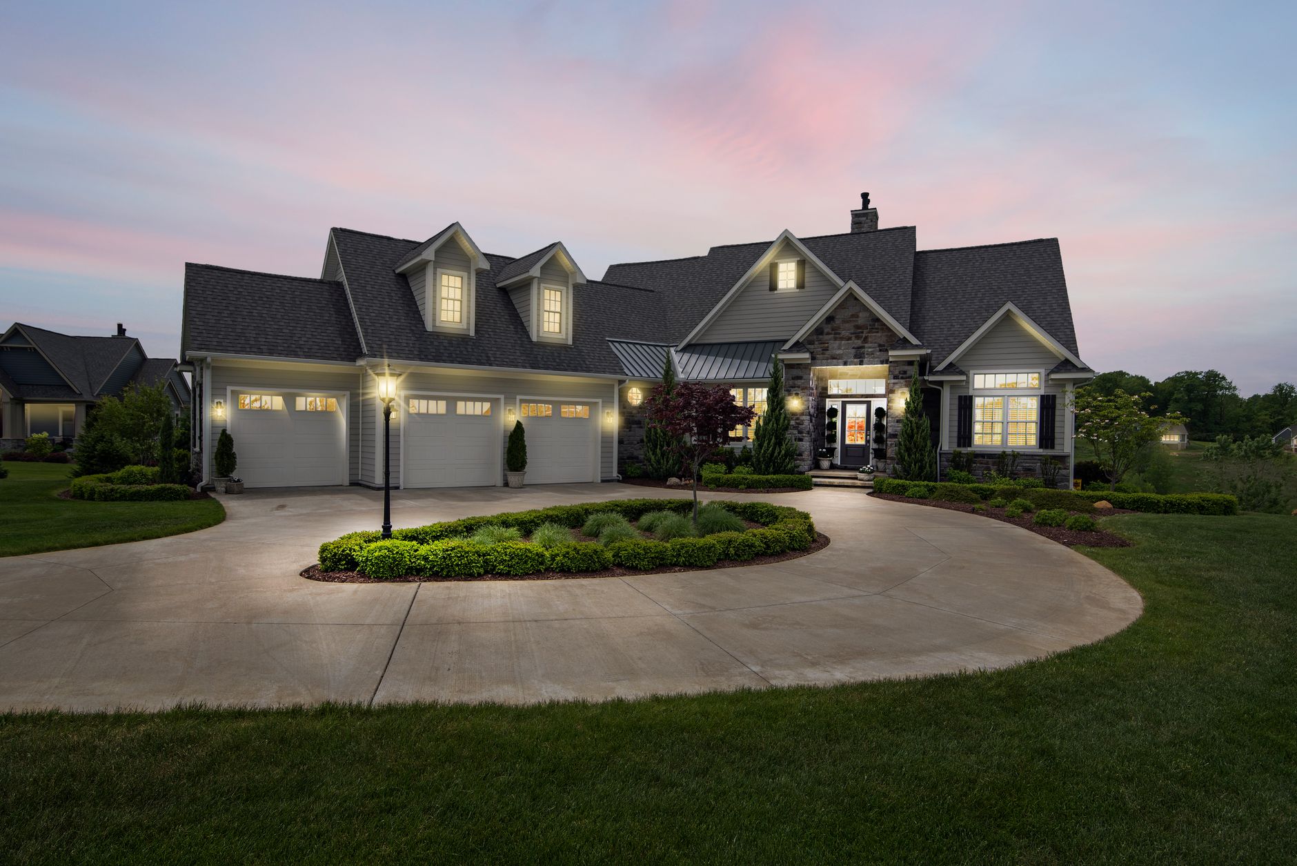 Craftsman-style home with lit windows and landscaped drive at dusk
