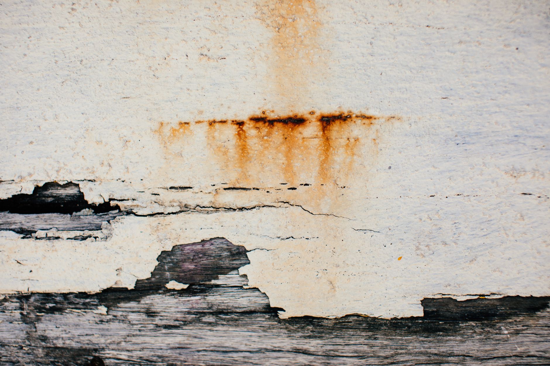 Rust-colored water staining and peeling paint running down a wall